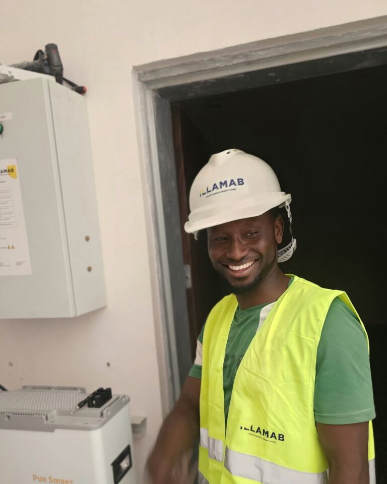 Illamab Energy Solutions technician wearing branded safety equipment beside inverter and battery installation